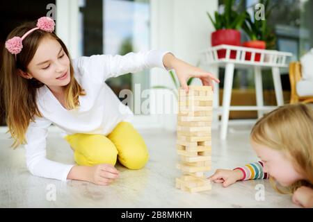 Zwei niedliche Schwestern, die zu Hause Holzklötze spielen, spielen ein Tower-Spiel. Kinder, die ihre körperlichen und geistigen Fähigkeiten ausüben. Lustige Gesellschaftsspiele für Familienurlaub. Bleib bei Stockfoto