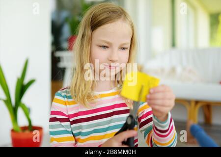 Junges Mädchen, das zu Hause buntes Papier mit einer Schere schneidet. Kreatives Kind macht Handwerk. Bildung und Fernunterricht für Kinder. Homeschooling während qua Stockfoto