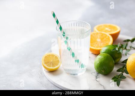 Frisches Zitruwasser mit Zitronensaft. Sauberes Wasser aus Glas mit Trinkinstroh und Zitrone auf Marmorgrund Stockfoto