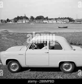 1950, historisch, ein Tag draußen...eine Dame, die auf dem Beifahrersitz eines beliebten Autos der Epoche sitzt, ein zweitüriger Ford Anglia 100E, neben dem Fluss Frome, in der Nähe von Old Sodbury, England, Großbritannien. Stockfoto