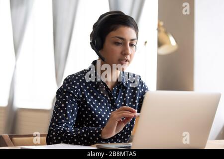 Seriöse Inderin, die Kopfhörer mit einem Laptop trägt Stockfoto