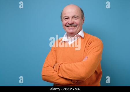 Lächelnd reif casual Mann in orange Pullover isoliert auf blau Hintergrund Stockfoto