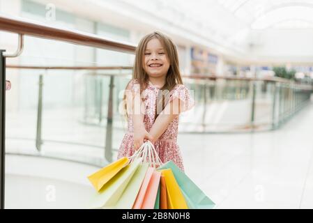 Ein kleines Mädchen hält mehrfarbige Pastelltaschen in den Händen. Das Konzept des Einkaufs, des Einkaufs im Einkaufszentrum. Stockfoto