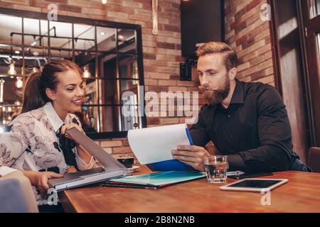 Junge Geschäftsleute arbeiten an Papierarbeiten zusammen und sprechen über Berichte und Finanzen. Porträt des jungen Geschäftsmannes und der Frau, die in Café A sitzen Stockfoto