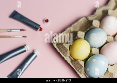 Das Konzept, Ostereier in pastellfarbenen Wasserfarben zu färben. Farben und Bürsten zum Färben von Eiern für Ostern auf pinkfarbenem Hintergrund. Stockfoto