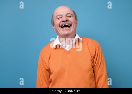 Senior hispanic Mann in orange Pullover lachend über Witz. Stockfoto