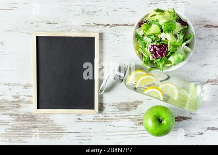 Salat, Wasser und apfel mit Tafel für Text Draufsicht auf Holzhintergrund. Gesundes Essen, Ernährungskonzept. Diät-Planung. Stockfoto
