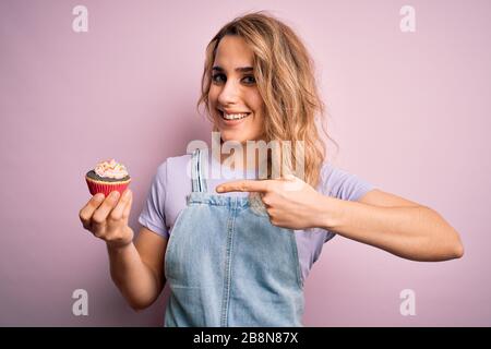 Junge schöne blonde Frau Eatimg Schokoladenkuchen über isoliertem rosafarbenem Hintergrund sehr glücklich mit Hand und Finger Stockfoto