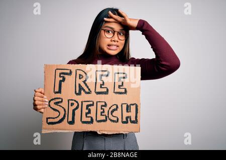 Asiatisches Mädchen, das um Rechte bittet, die Banner mit freier Sprachnachricht über weißem Hintergrund halten, der mit der Hand am Kopf betont wurde, schockiert mit Scham und Überraschung Stockfoto