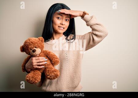 Junge schöne chinesische Frau mit Teddybär stehend über isoliert weißer Hintergrund mit Hand betonte am Kopf, mit Scham und Überraschung schockiert f Stockfoto