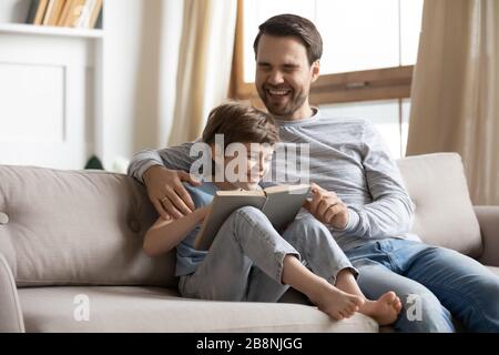 Lächelnder junger Vater und kleiner Sohn lesen Buch zusammen Stockfoto