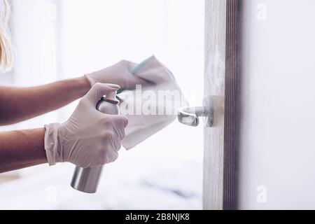 Die Frau desinfiziert den Türgriff mit einer Desinfektionsflüssigkeit. Stockfoto