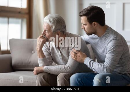 Liebevoller erwachsener Sohn umarmt Unterstützung verärgerter älterer Vater Stockfoto