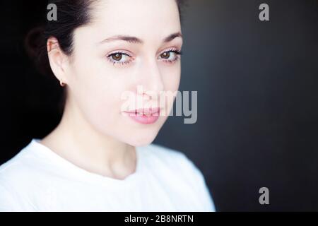 Fröhliches Mädchen lächelnd. Beauty-Porträt junge fröhliche positive Brunette-Frau auf schwarzem Hintergrund isoliert. Europäische Frau mit Kopfschuss. Positive menschliche Emotionen Gesichtsausdruck Körpersprache Stockfoto