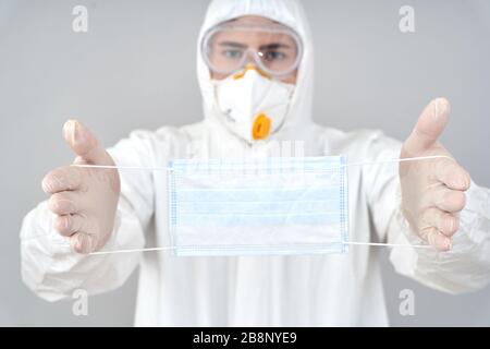 Arzt in schützender Arbeitskleidung hält Sicherheit Gesichtsmaske in den Händen Stockfoto