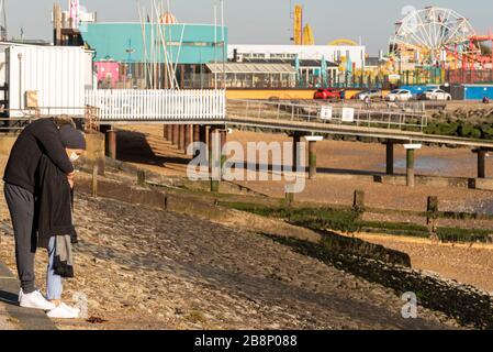 Junge Paare, die Gesichtsmasken an der Küste von Southend tragen, sorgten sich wegen der COVID-19-Coronavirus-Pandemie für ihre Zukunft. Schützende Umarmung Stockfoto