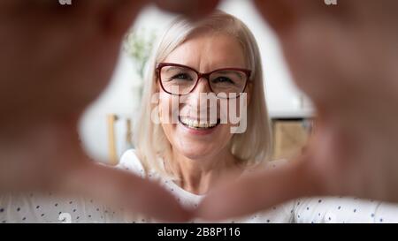 Glückliche ältere Frau in Brillen, die Herzsymbol macht. Stockfoto