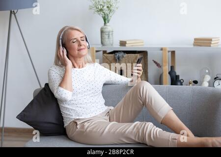 In voller Länge friedliche, pensionierte Dame, die Lieblingsmusik in Ohrhörern genießt. Stockfoto