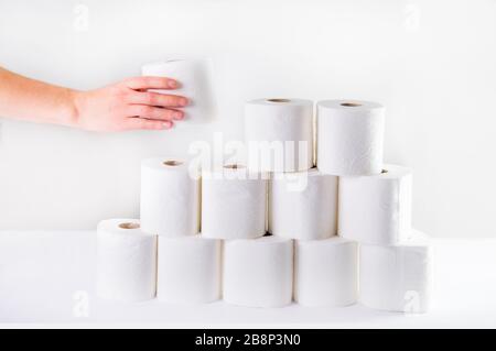 Eine männliche Hand nimmt eine Rolle Toilettenpapier aus einem gefalteten Turm mit toilettenrollen auf weißem Grund. Mangelndes Konzept für Krisenprodukte Stockfoto