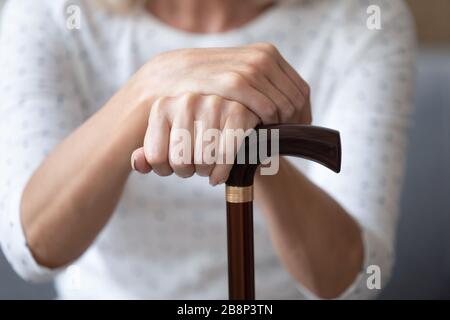 Schließen Sie ältere Frauen, die zerknitterte Hände auf einem Holzfußstab halten. Stockfoto