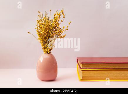 Ein wunderschöner Frühlings-Blumenstrauß aus frischer Mimosa in einer rosafarbenen Porzellanvase in Form eines Eies auf weichem rosa Hintergrund mit zwei Jahrbüchern in einem harten Stockfoto