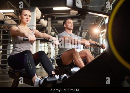 Niedrige Winkelansicht bei sportlichen Paaren, die Trainingsgeräte während des Krafttrainings in einem modernen Fitnessstudio verwenden, Platz kopieren Stockfoto