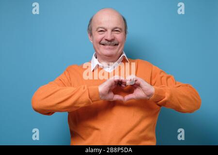 Reifer Mann zeigt Herz mit Fingern im Studio Stockfoto