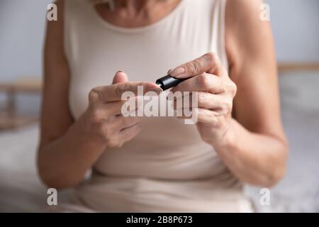 Ältere Frau, die allein zu Hause ein Blutzucker-Messgerät verwendet. Stockfoto