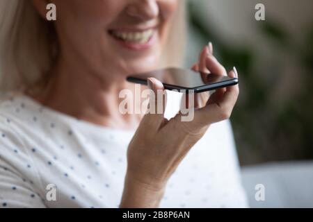 Glückliche ältere Frau mit Spracherkennungsfunktion oder virtuellem Assistenten. Stockfoto