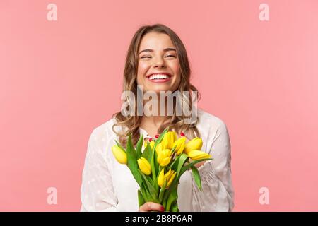 Frühlings-, Glücks- und Festkonzept. Nahaufnahme des glücklichen und unbeschwerten blonden europäischen Mädchens erhalten einen schönen Blumenstrauß, der gelb gehalten wird Stockfoto