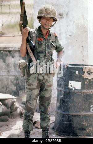 1968, Danang, Vietnam, authentisches Foto eines südvietnamesischen Soldaten, der in Vietnam eine Waffe neben Trommeln mit Chemikalien hält Stockfoto