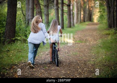 Mutter nimmt sein Kind für Fahrradtour. Hilfe bei einer ersten Fahrt auf dem Fahrrad. Stockfoto