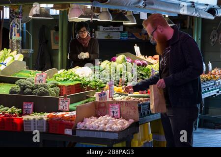 Judi Albayalde hilft mit Manzo Brothers Produce einem Kunden am Pike Place Market am Sonntag, 22. März 2020. Während viele der Lebensmittelgeschäfte offen sind, sind die nicht essentiellen Geschäfte des Wahrzeichen vorübergehend geschlossen, einschließlich der allgegenwärtigen Souvenir- und Blumenbuden des Marktes. Stockfoto