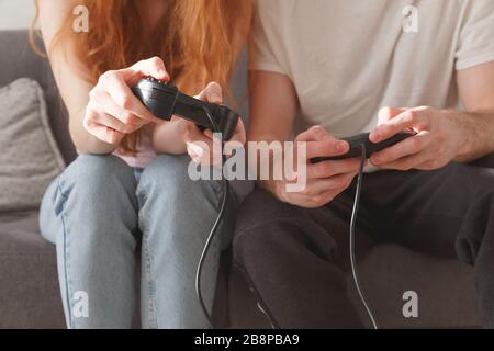 Ein junges Paar ein Mädchen und ein Kerl mit Joysticks in den Händen spielen auf der Konsole, während sie auf der Couch sitzen. Stockfoto