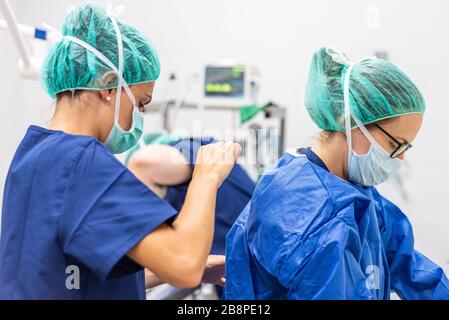 Medizinischer Assistent hilft einem Chirurgen, sterile Kleidung in einem Operationssaal anzubringen. Stockfoto