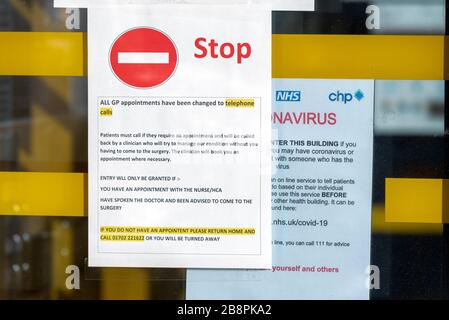 Coronavirus Warnhinweis am Fenster des Eingangs zur Arztpraxis in Westcliff on Sea, Essex, Großbritannien, mit der Bitte, dass mögliche Erkrankte nicht einreisen. Geh nach Hause 111 Stockfoto