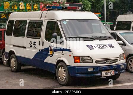 Chongqing, China - 9. Mai 2010: Stadtzentrum. Nahaufnahme des weißen Parket Police Transporters mit grünem Laub im Rücken. Teile anderer Autos und gelbe Mandarinensymbole Stockfoto