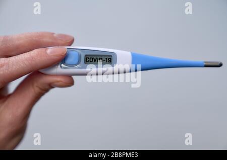 Weibliche Hand hält klinisches Thermometer mit Kovid 19-Text auf dem Bildschirm während der globalen Kovid 19- oder Corona-Pandemie Stockfoto