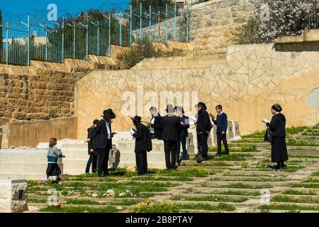 Eine Gruppe von orthodoxen Juden, die auf einem Friedhof auf dem Ölberg, Jerusalem, Israel und dem Nahen Osten beten. Stockfoto