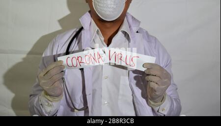 Ein Arzt trägt eine Gesundheitsmaske und ein auf weißem Hintergrund isoliertes Poke-Papier-Corona-Virus. Stockfoto