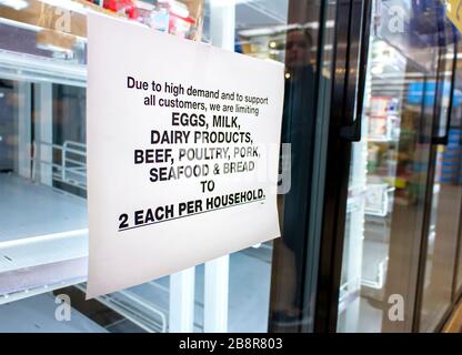 Coronavirus-bezogene Zeichen rationieren Lebensmittel wie Milchprodukte, Fleisch, Meeresfrüchte, Brot und Eier in einem Supermarkt. Die Regale des Kühlers sind ziemlich emp Stockfoto