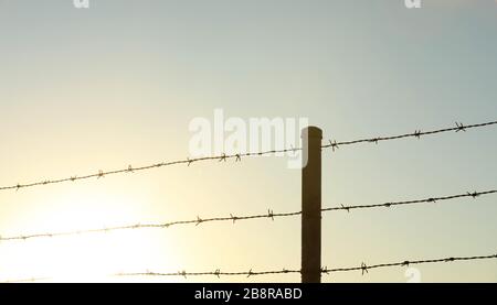 Sonnenaufgang brannte in der Ecke aus. Stachelbarbendrahtzäune und Zaunpfosten. Hoffnung und Positivität Stockfoto