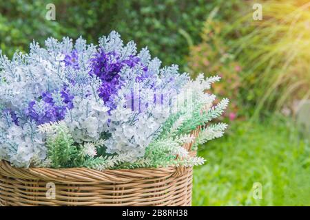 Künstlicher Blumenstrauß in Korbkörben im schönen Garten. Stockfoto