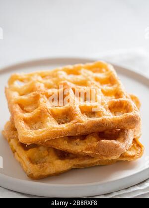 Perfekte herzhafte Keto Waffeln. Zwei Zutaten verkaffeln sich auf dem Teller über weißem Marmorhintergrund. Eier und Parmesankäse mit niedrigen Karb-Waffeln. Extreme Nahaufnahme. Vertikal. Stockfoto