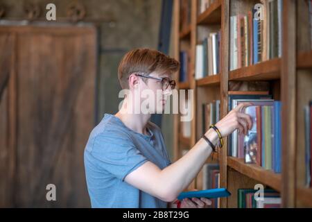 Junger Mann in Brille, der ein Buch aus einem Bücherregal nimmt Stockfoto