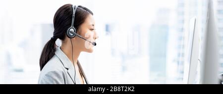 Junge asiatische Geschäftsfrau, die Headsets trägt, die als Kundendienstanbieter im Callcenter City Office Banner-Hintergrund arbeiten Stockfoto