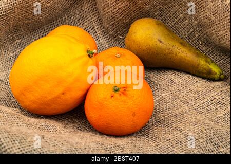 Zitrone, Mandarinen und Birne auf einem Hintergrund aus strukturiertem Stoff. Nahaufnahme Stockfoto