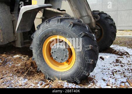 Schwarz-gelbes Traktorrad mit kräftiger Lauffläche auf dem Reifen steht auf gefrorenem Boden mit Schnee. Stockfoto