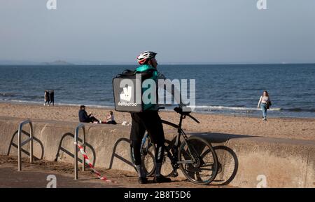 Deliveroo Cycliste Delivery man in Foreground and People on Portobello Beach during the Coronavirus Outbreak 2020, Edinburgh, Scotland, UK, Stockfoto