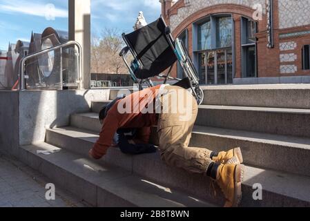 Behinderter Latino-junger Mann im Rollstuhl fällt eine Treppe hinunter, die er nicht mit dem Stuhl auf der Straße hinuntergehen kann Stockfoto